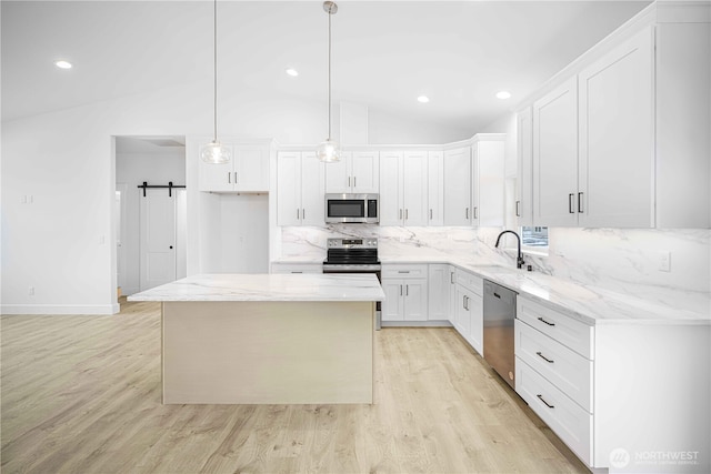 kitchen with stainless steel appliances, a barn door, a kitchen island, and white cabinets