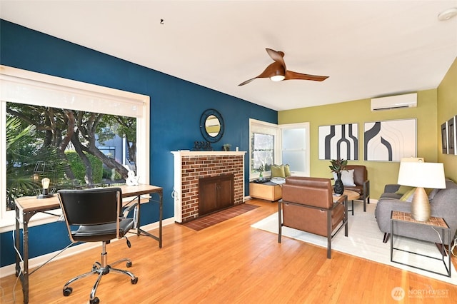 living room with a ceiling fan, a brick fireplace, an AC wall unit, wood finished floors, and baseboards