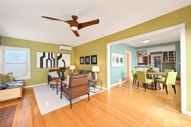 living room featuring a ceiling fan, baseboards, a wall unit AC, and light wood finished floors