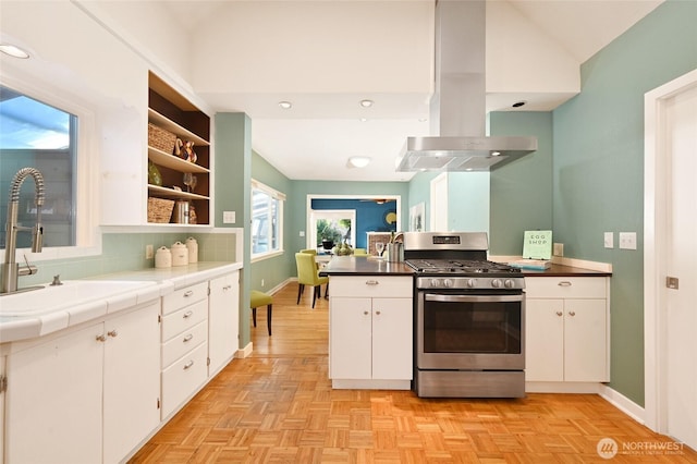 kitchen with tile counters, stainless steel gas range oven, white cabinets, and island range hood