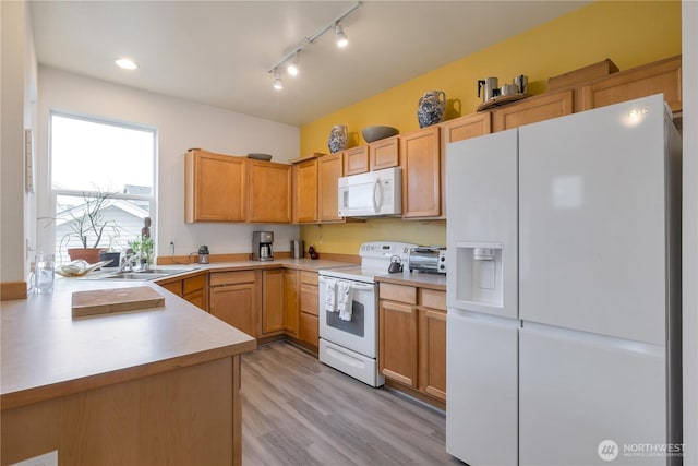 kitchen with a peninsula, white appliances, a sink, light countertops, and light wood finished floors