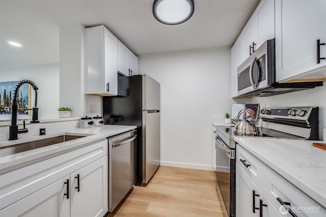 kitchen featuring light wood-type flooring, white cabinetry, appliances with stainless steel finishes, and a sink