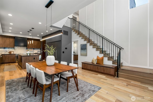 dining space with light wood-style flooring, a decorative wall, recessed lighting, visible vents, and stairway