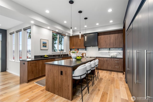 kitchen with dark countertops, hanging light fixtures, a kitchen island, wall chimney range hood, and modern cabinets