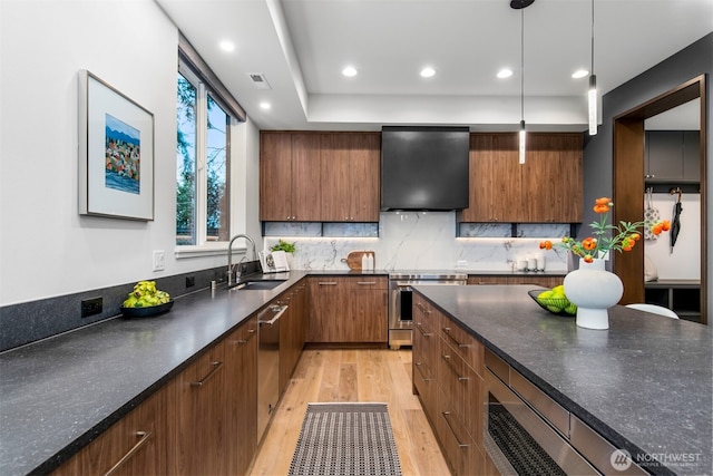 kitchen featuring stainless steel appliances, a sink, wall chimney range hood, dark countertops, and pendant lighting