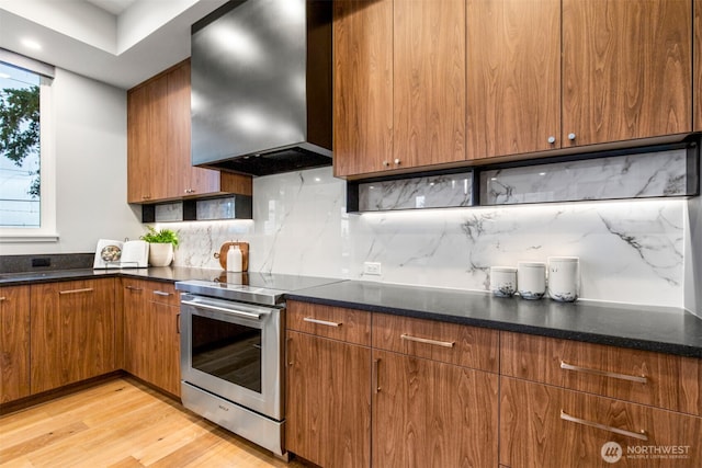 kitchen with electric stove, dark countertops, backsplash, brown cabinetry, and extractor fan