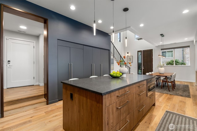 kitchen with brown cabinetry, dark countertops, modern cabinets, decorative light fixtures, and a center island