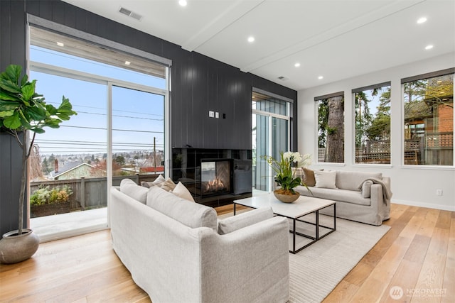 living room featuring light wood-style floors, a healthy amount of sunlight, visible vents, and a multi sided fireplace