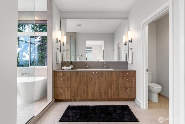 full bath with baseboards, visible vents, toilet, vanity, and a freestanding tub