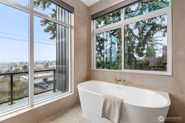 full bath with tile patterned flooring, a freestanding bath, and tile walls