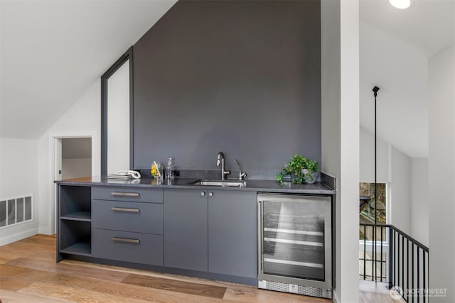 bar featuring lofted ceiling, visible vents, a sink, light wood-type flooring, and beverage cooler