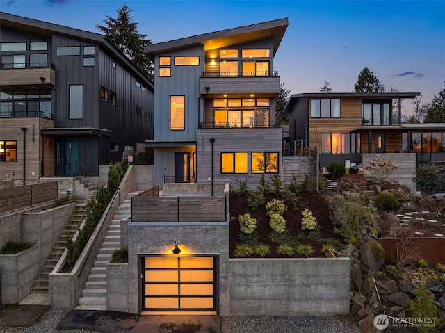 back of house at dusk with board and batten siding, stairs, and a balcony