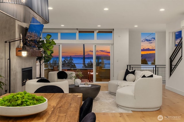 living area featuring a large fireplace, a wall of windows, stairs, recessed lighting, and wood finished floors