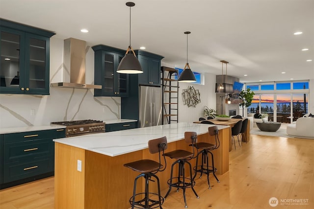 kitchen featuring a wall of windows, light wood-style floors, wall chimney exhaust hood, premium appliances, and backsplash