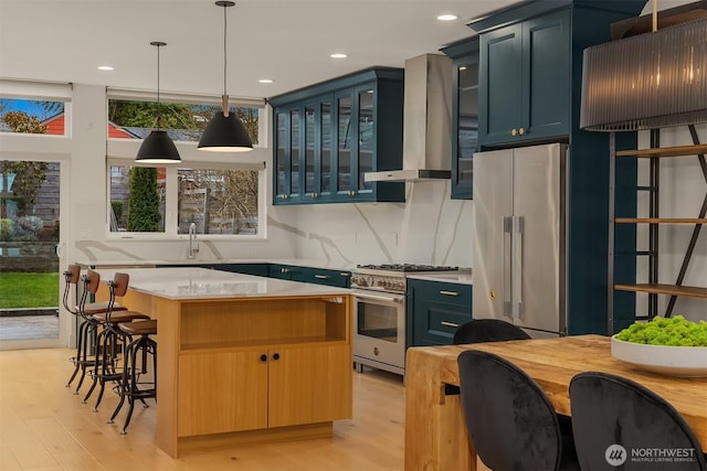 kitchen featuring a sink, premium appliances, a kitchen island, wall chimney exhaust hood, and light countertops