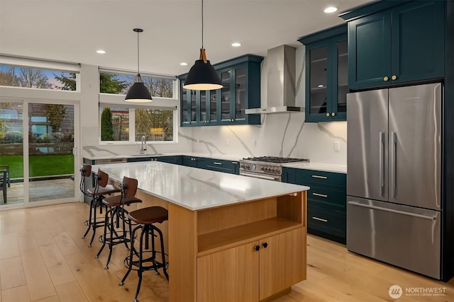 kitchen with a kitchen breakfast bar, high end appliances, light wood-style floors, wall chimney exhaust hood, and a sink