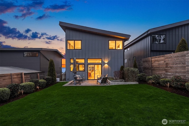 back of property at dusk with a patio area, a fenced backyard, board and batten siding, and a yard