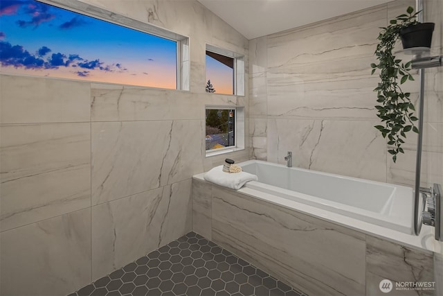 bathroom with lofted ceiling, a bath, and tile walls