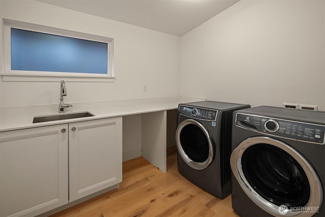 washroom featuring light wood finished floors, cabinet space, independent washer and dryer, and a sink