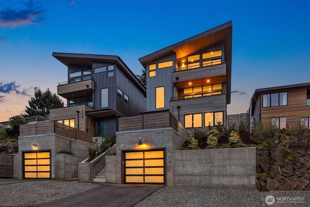 contemporary home with a garage, board and batten siding, gravel driveway, and a balcony