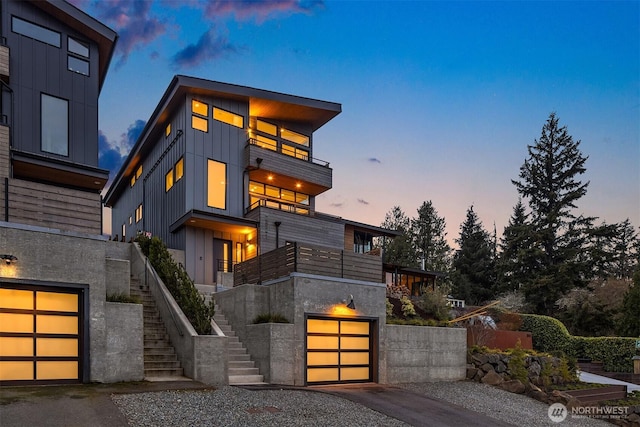 contemporary home featuring driveway, stairway, board and batten siding, a garage, and a balcony