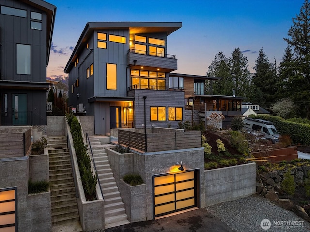 contemporary house with board and batten siding, stairs, driveway, a balcony, and an attached garage