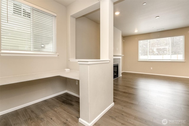 unfurnished living room featuring wood finished floors, built in study area, a glass covered fireplace, and baseboards