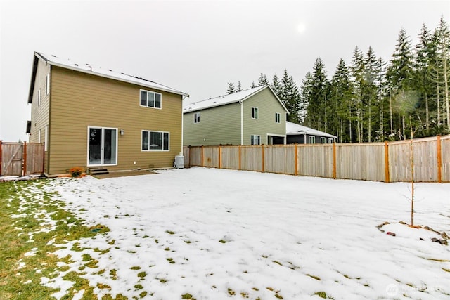 snow covered house featuring entry steps, central AC, and a fenced backyard