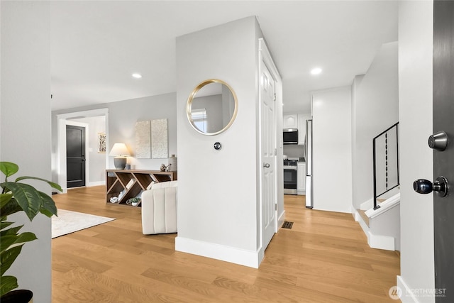 hall featuring light wood-style floors, recessed lighting, baseboards, and stairs