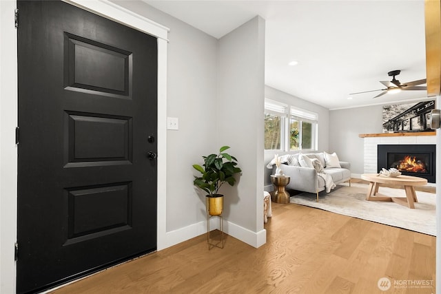 foyer entrance with light wood-type flooring, a fireplace, baseboards, and a ceiling fan