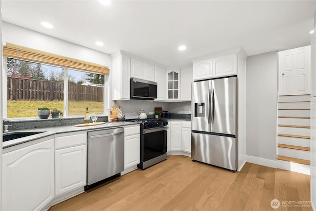 kitchen with stainless steel appliances, a sink, glass insert cabinets, and white cabinetry