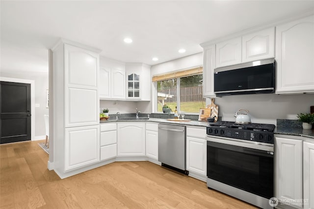 kitchen with appliances with stainless steel finishes, glass insert cabinets, and white cabinetry