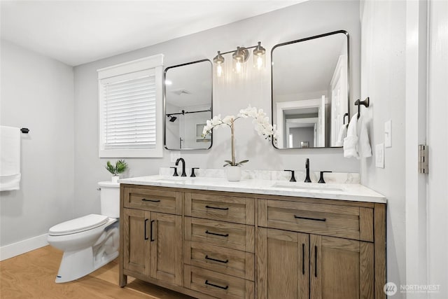 full bath with double vanity, wood finished floors, a sink, and toilet