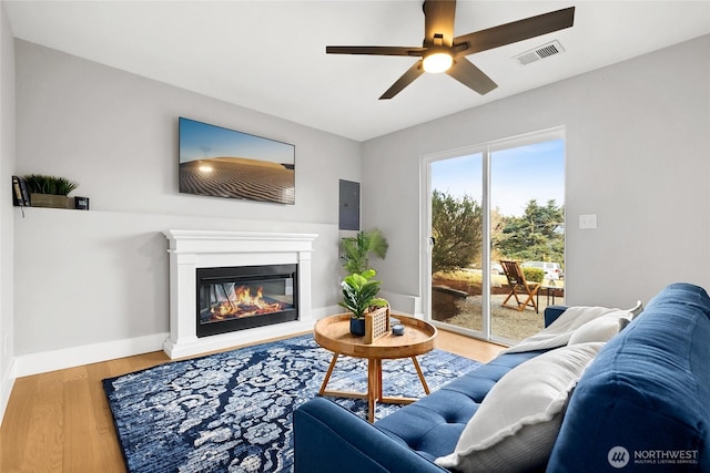 living area with visible vents, a glass covered fireplace, ceiling fan, wood finished floors, and baseboards