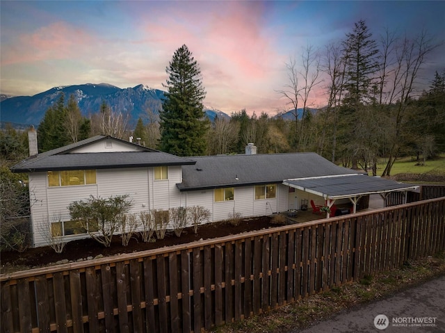 view of side of home with a chimney, a mountain view, and fence