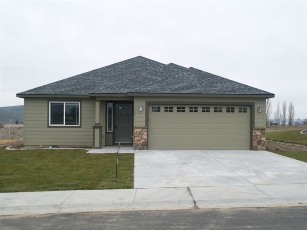 view of front of home featuring an attached garage, a front lawn, concrete driveway, and roof with shingles