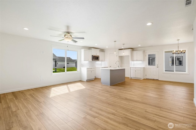 kitchen with stainless steel microwave, open floor plan, visible vents, and ceiling fan with notable chandelier