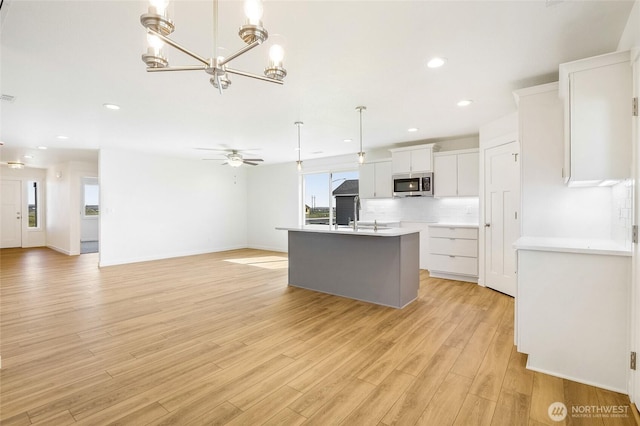 kitchen featuring white cabinets, a kitchen island with sink, light wood-style flooring, stainless steel microwave, and open floor plan