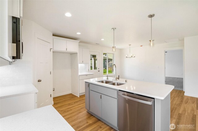 kitchen with stainless steel dishwasher, light wood-type flooring, light countertops, a sink, and a notable chandelier