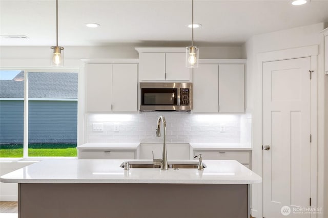 kitchen with a sink, stainless steel microwave, pendant lighting, and white cabinetry