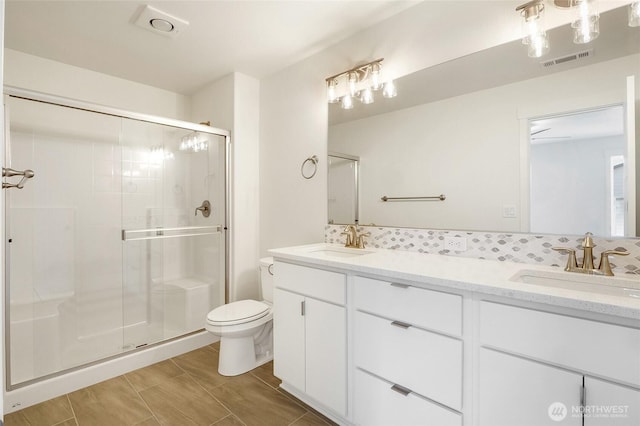full bathroom featuring visible vents, double vanity, toilet, a sink, and a stall shower