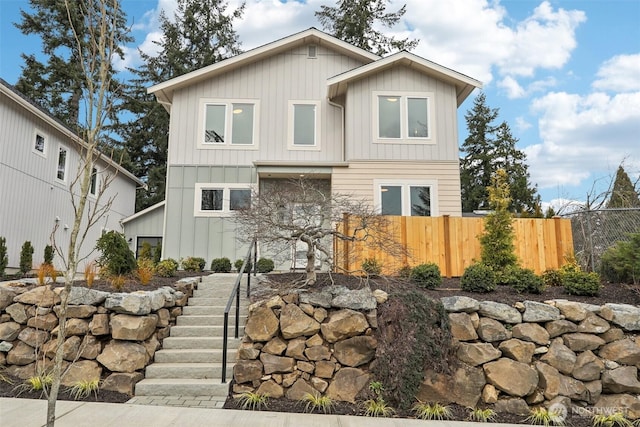 view of front facade with stairway, board and batten siding, and fence