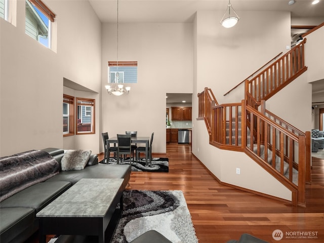 living area with a notable chandelier, a high ceiling, wood finished floors, baseboards, and stairs