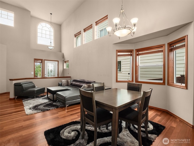 dining room with hardwood / wood-style flooring, a towering ceiling, baseboards, and an inviting chandelier