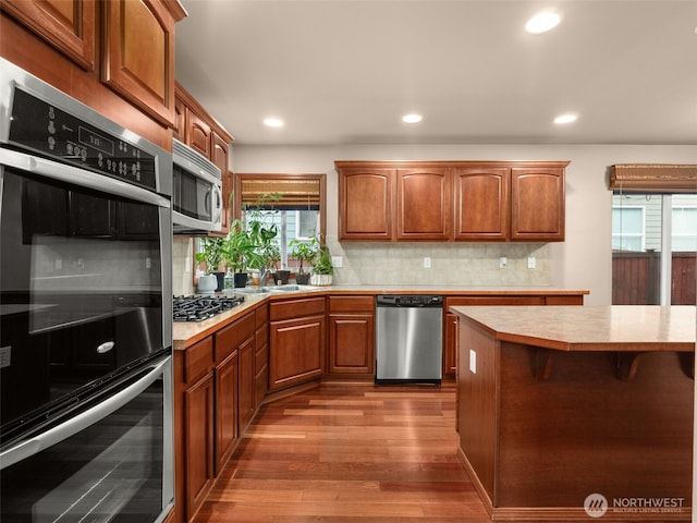 kitchen with light countertops, appliances with stainless steel finishes, brown cabinetry, and dark wood finished floors