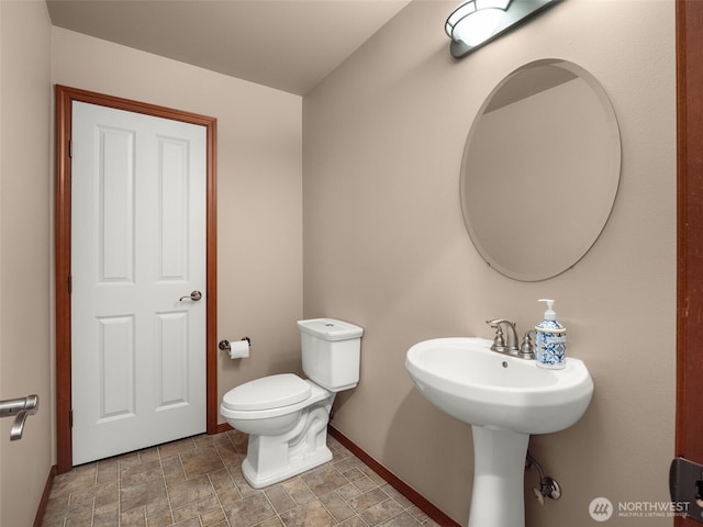 half bath with stone finish floor, toilet, and baseboards