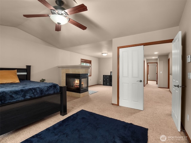 bedroom featuring a ceiling fan, a fireplace, vaulted ceiling, and light carpet