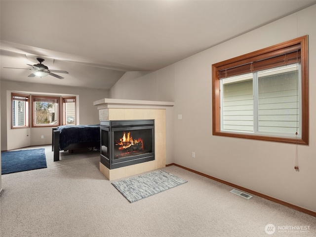 carpeted bedroom featuring ceiling fan, a tile fireplace, visible vents, baseboards, and vaulted ceiling