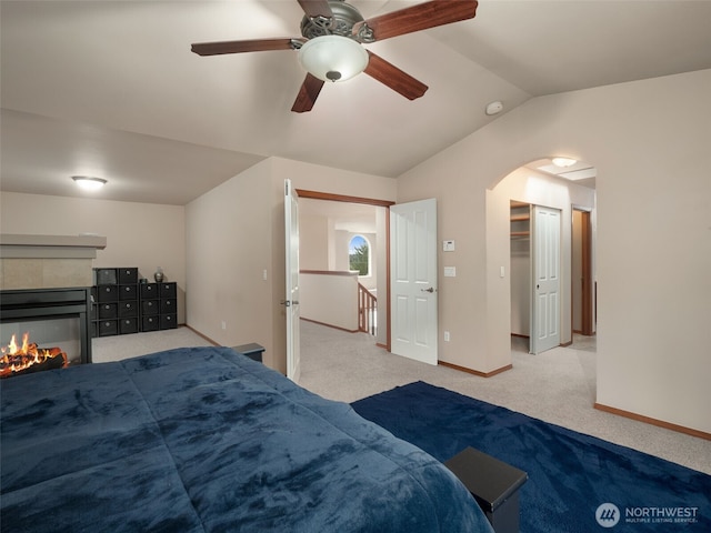 carpeted bedroom featuring baseboards, arched walkways, a ceiling fan, a tile fireplace, and vaulted ceiling