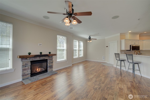 living area with baseboards, light wood finished floors, a fireplace, ceiling fan, and crown molding